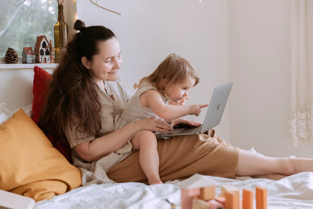 Bambino seduto sulle ginocchia della madre, che punta al computer portatile