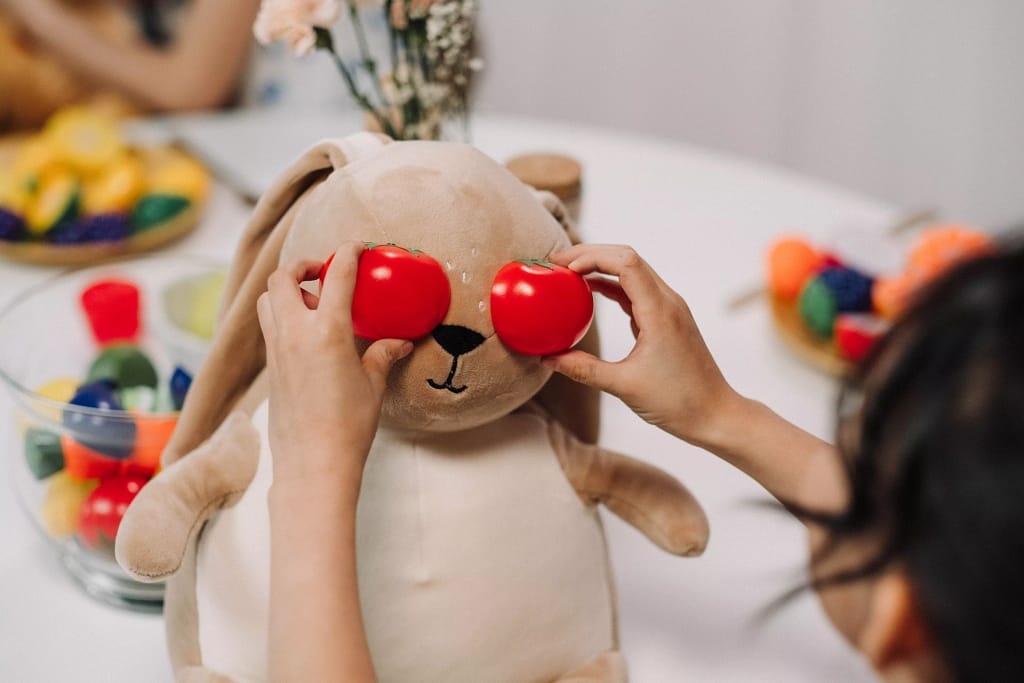 Child holding two toy tomatoes in front of stuffed animal's eyes